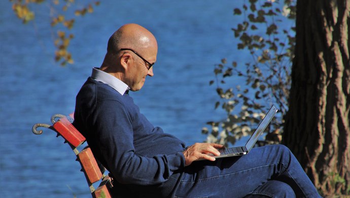 Man sitting on park bench with laptop near the water