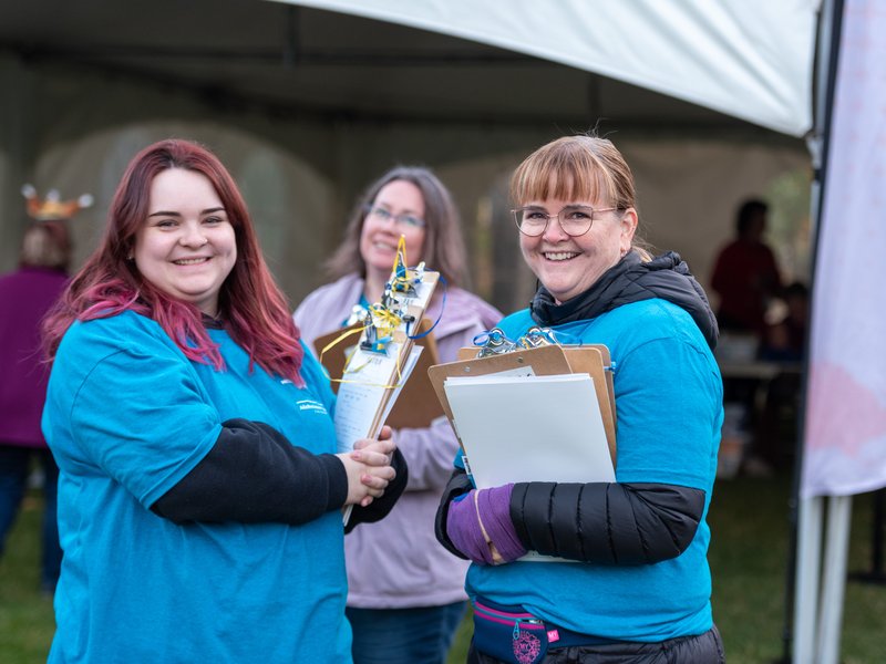 two people wearing blue shirts and holding clipboards smiling