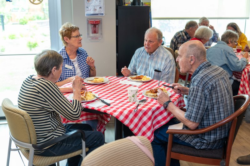 a group of seniors and care partners standing behind a table displaying their art