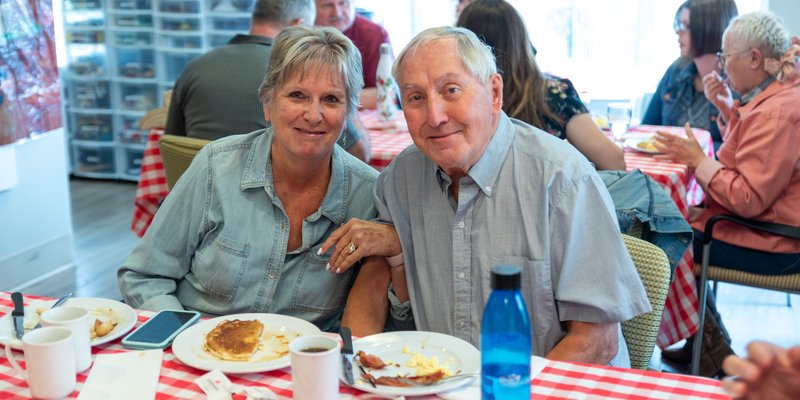 A senior couple linking arms at a breakfast table