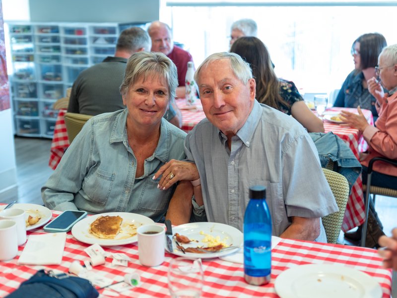 A senior couple linking arms at a breakfast table