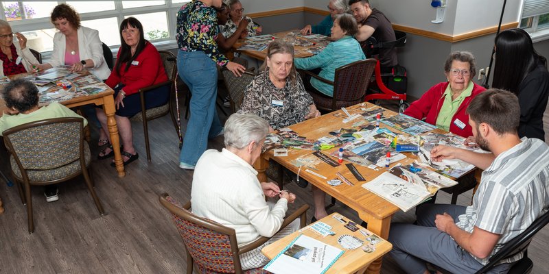 A group of seniors and helpers sitting at tables and making collages