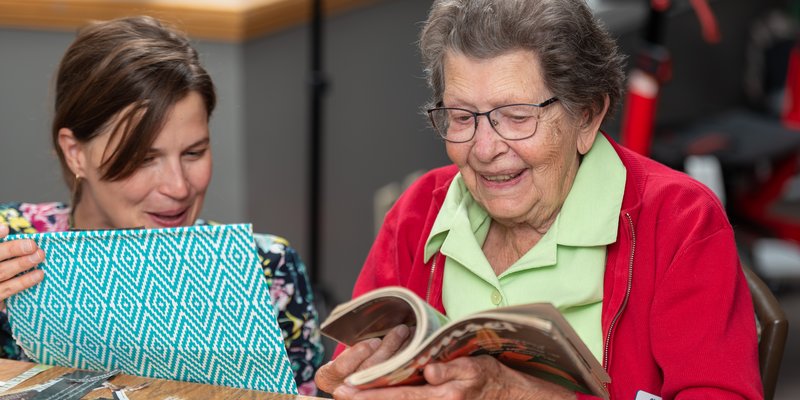 A senior and a helper looking through a magazine for collage images