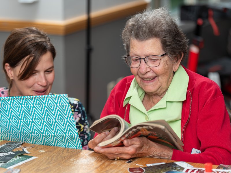 A senior and a helper looking through a magazine for collage images