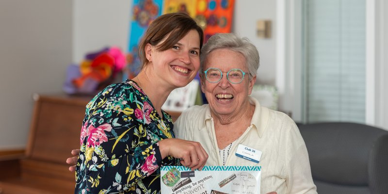 A senior and a helper holding a collage artwork and smiling