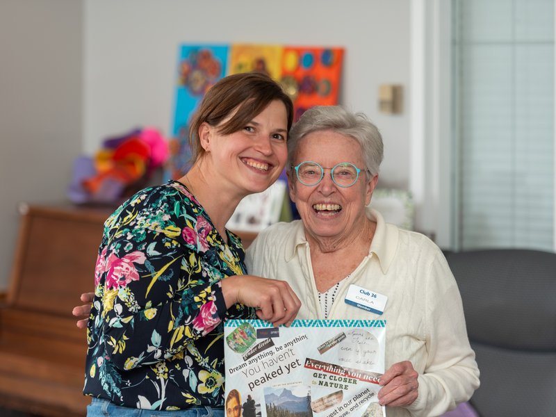 A senior and a helper holding a collage artwork and smiling