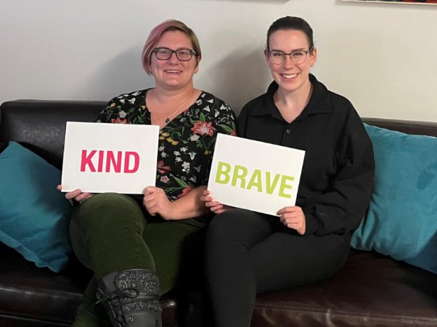 two people holding signs that say kind and brave