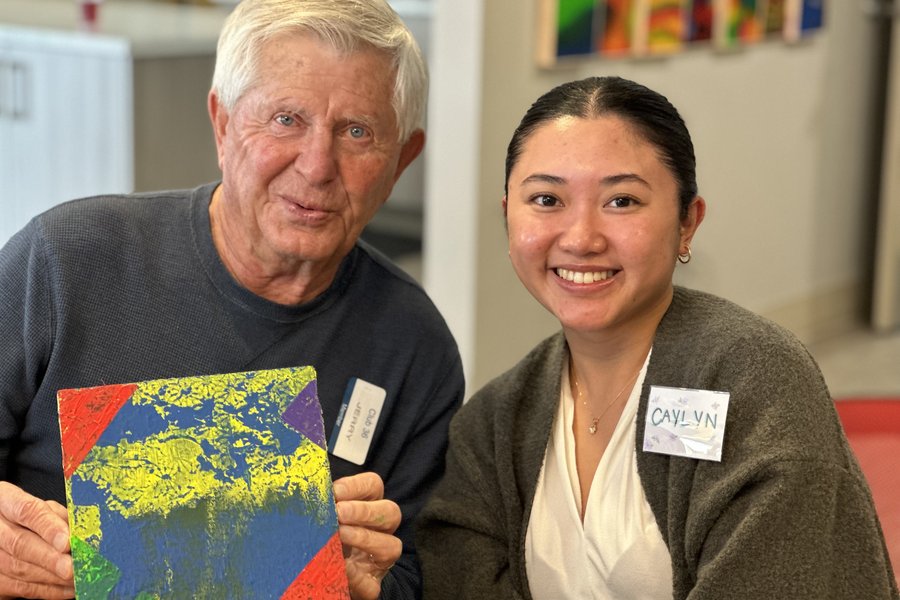 a senior smiling and holding a painter next to a smiling care partner