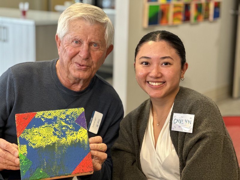 a senior smiling and holding a painter next to a smiling care partner