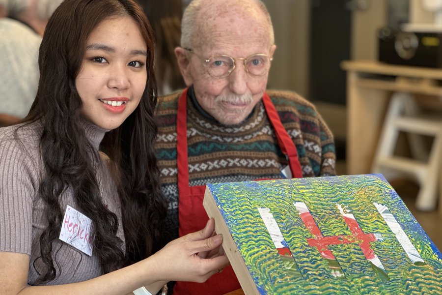 a care giver and a senior sitting together and smiling while displaying a painting
