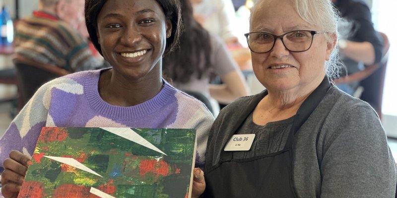 a care giver and a senior sitting together and smiling while displaying a painting