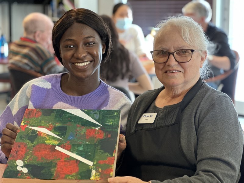 a care giver and a senior sitting together and smiling while displaying a painting
