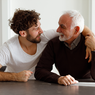 a younger and older man embracing from the side and smiling at each other
