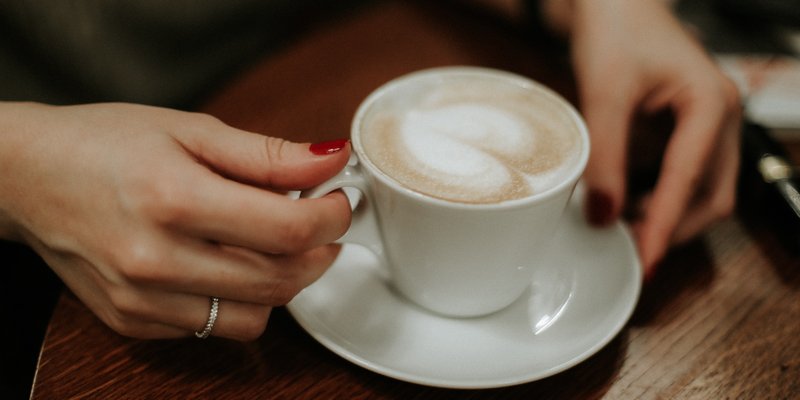 hands holding a latte on a table