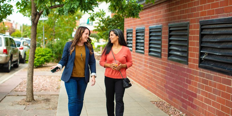 two people talking as they walk down the sidewalk