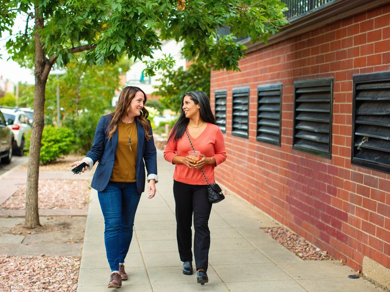 two people talking as they walk down the sidewalk