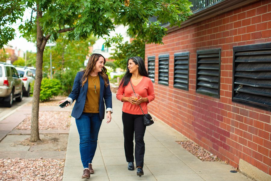 two people talking as they walk down the sidewalk