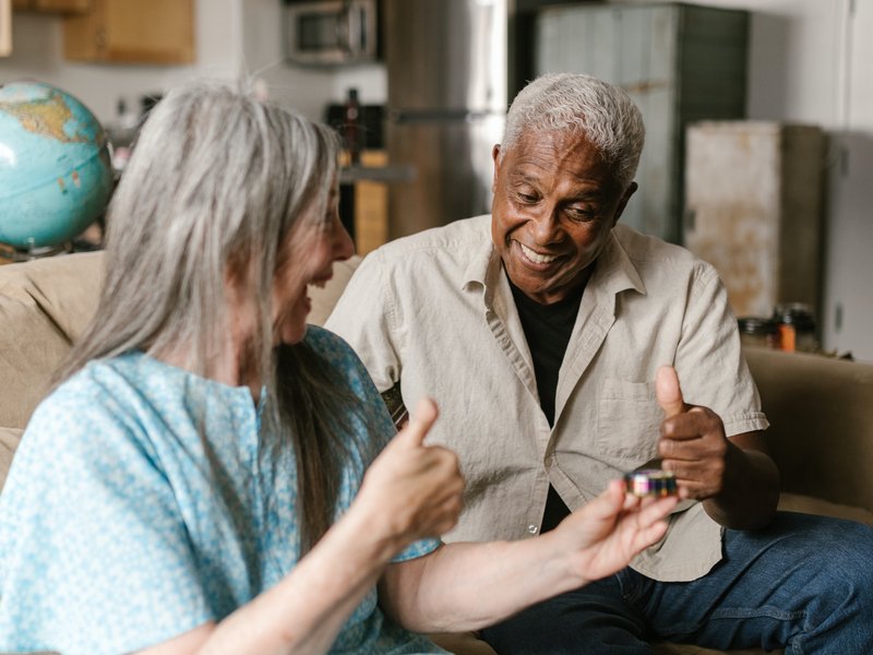 two senior smiling and talking on a couch